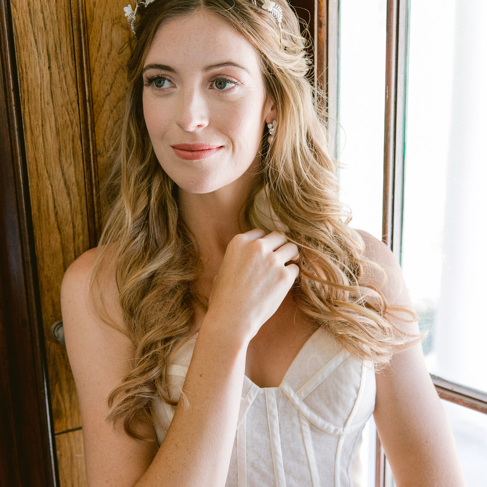 bride lining against a window wearing silver leaf and flower tiara with pearls and crystal stud earrings 